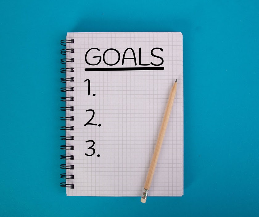 Notebook with pencil resting on it and "Goals" written on top with 1, 2, 3, underneath 